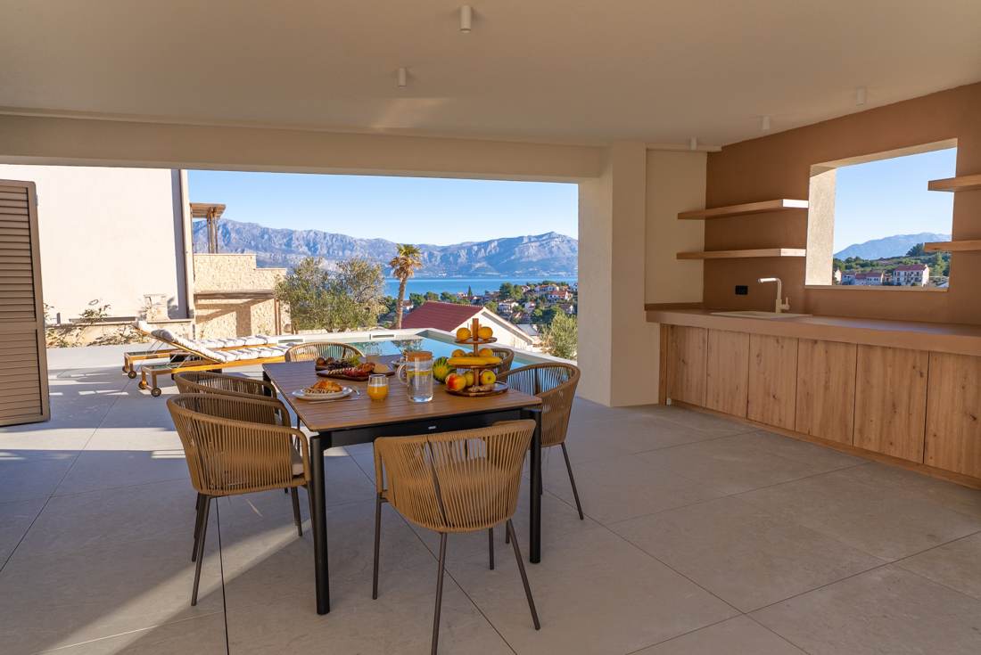 Covered outdoor dining area and kitchen overlooking the pool and sea